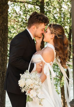 Intimate wedding portrait under a lush tree canopy with white floral bouquet.