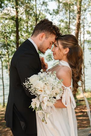 An intimate wedding moment captured in a wooded setting with white flowers and formal attire.