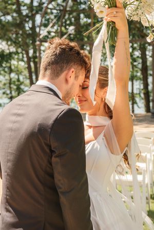 A couple shares an intimate moment at their outdoor wedding ceremony as the bride holds a bouquet overhead.