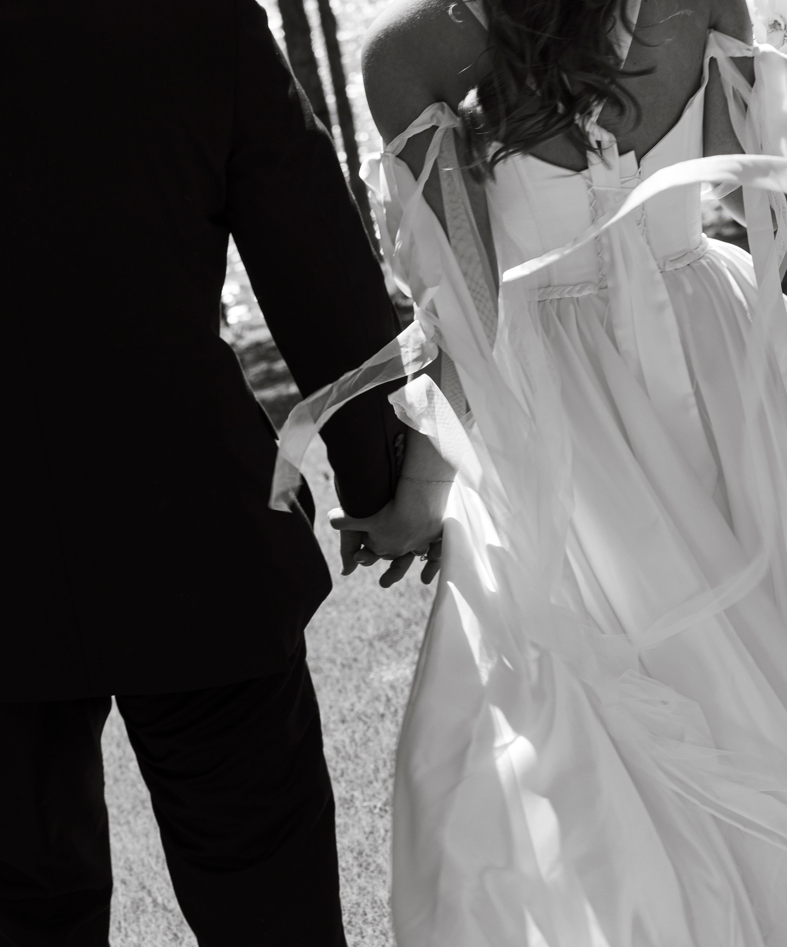 Black and white artistic photo showing bride and groom holding hands with flowing wedding dress.