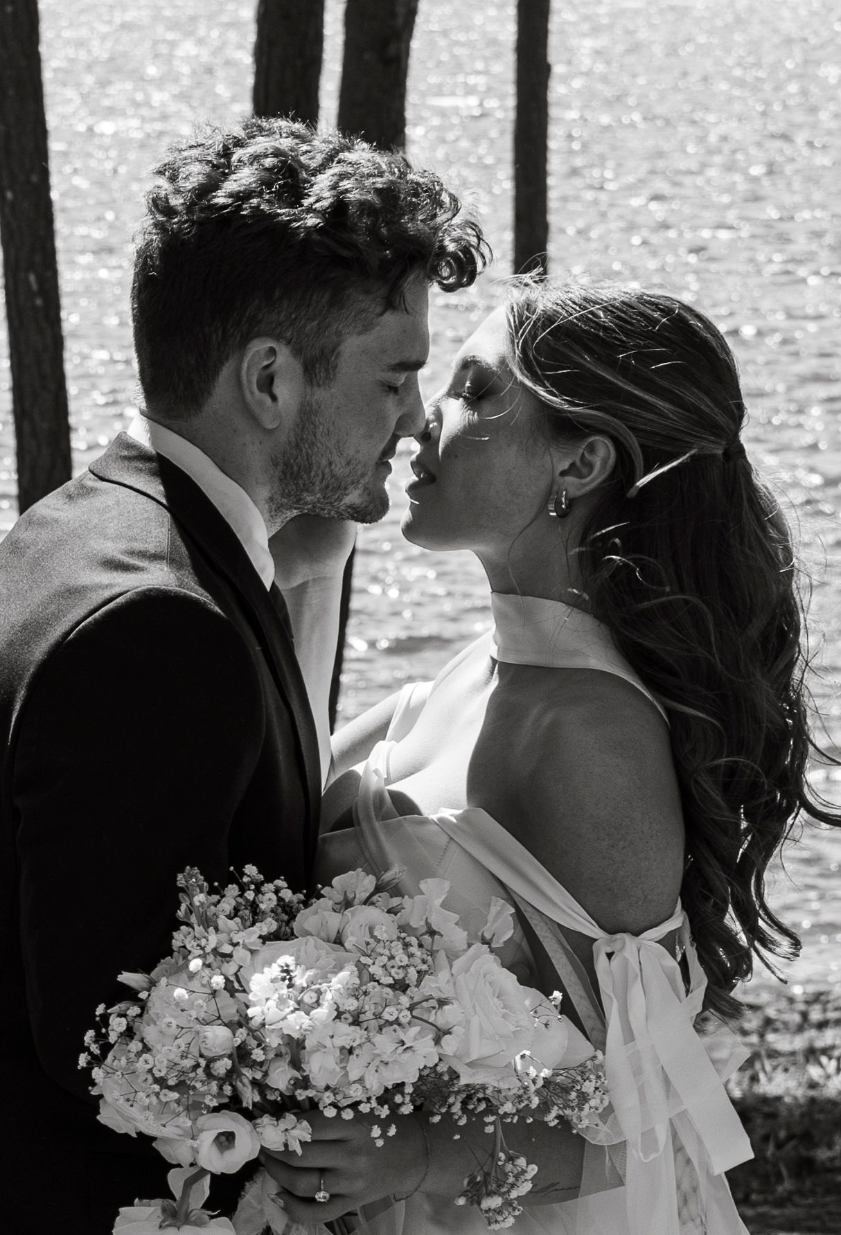 Black and white romantic wedding portrait with a delicate bouquet of flowers by the waterfront.