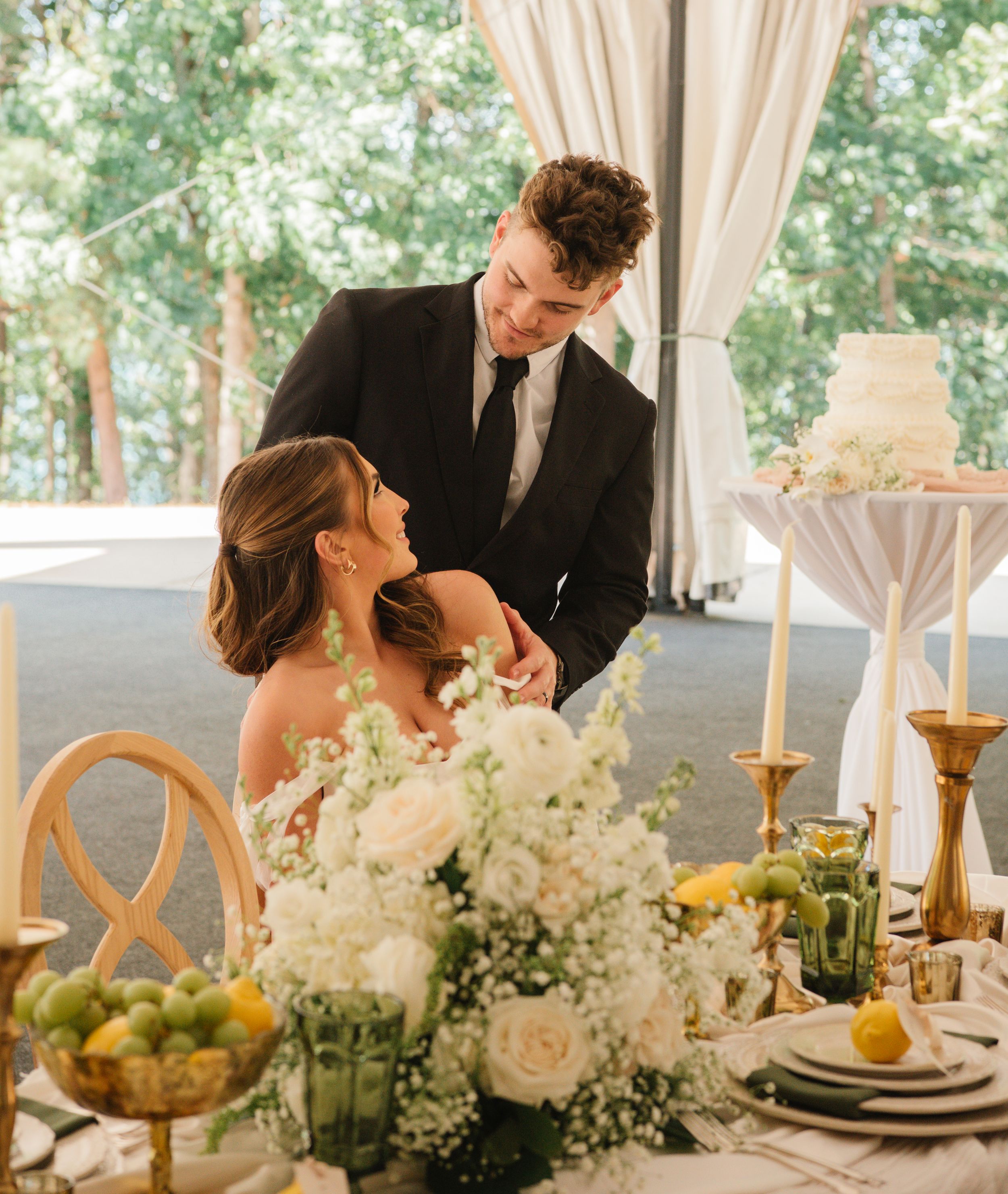 A romantic wedding reception table decorated with white flowers, candlesticks, citrus fruits and elegant place settings.