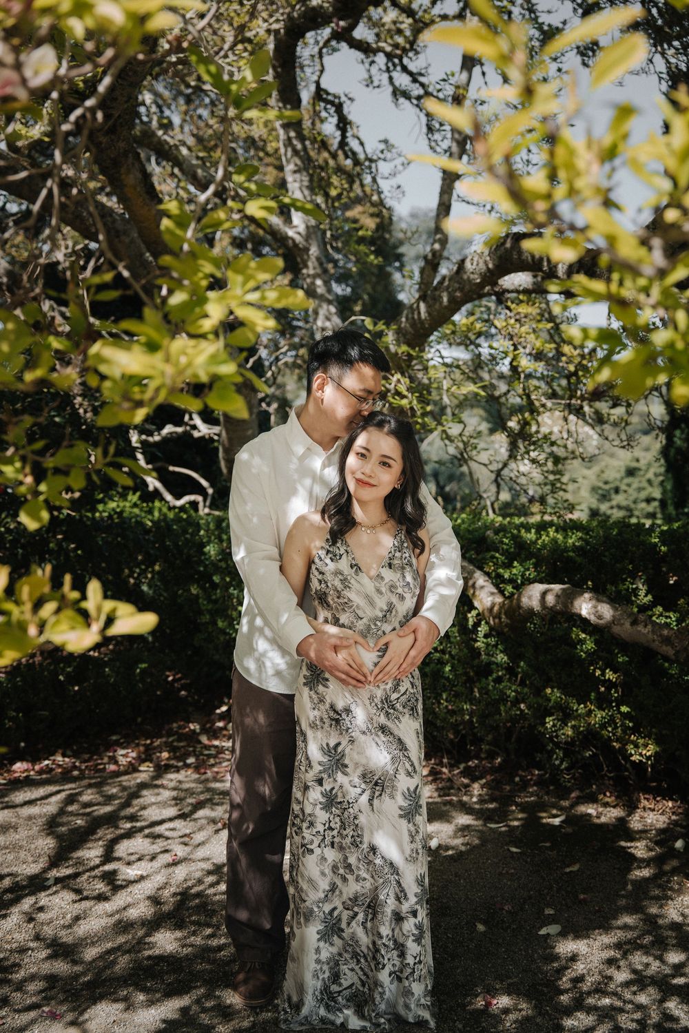 Intimate garden photoshoot under flowering trees with dappled sunlight creating natural shadows.