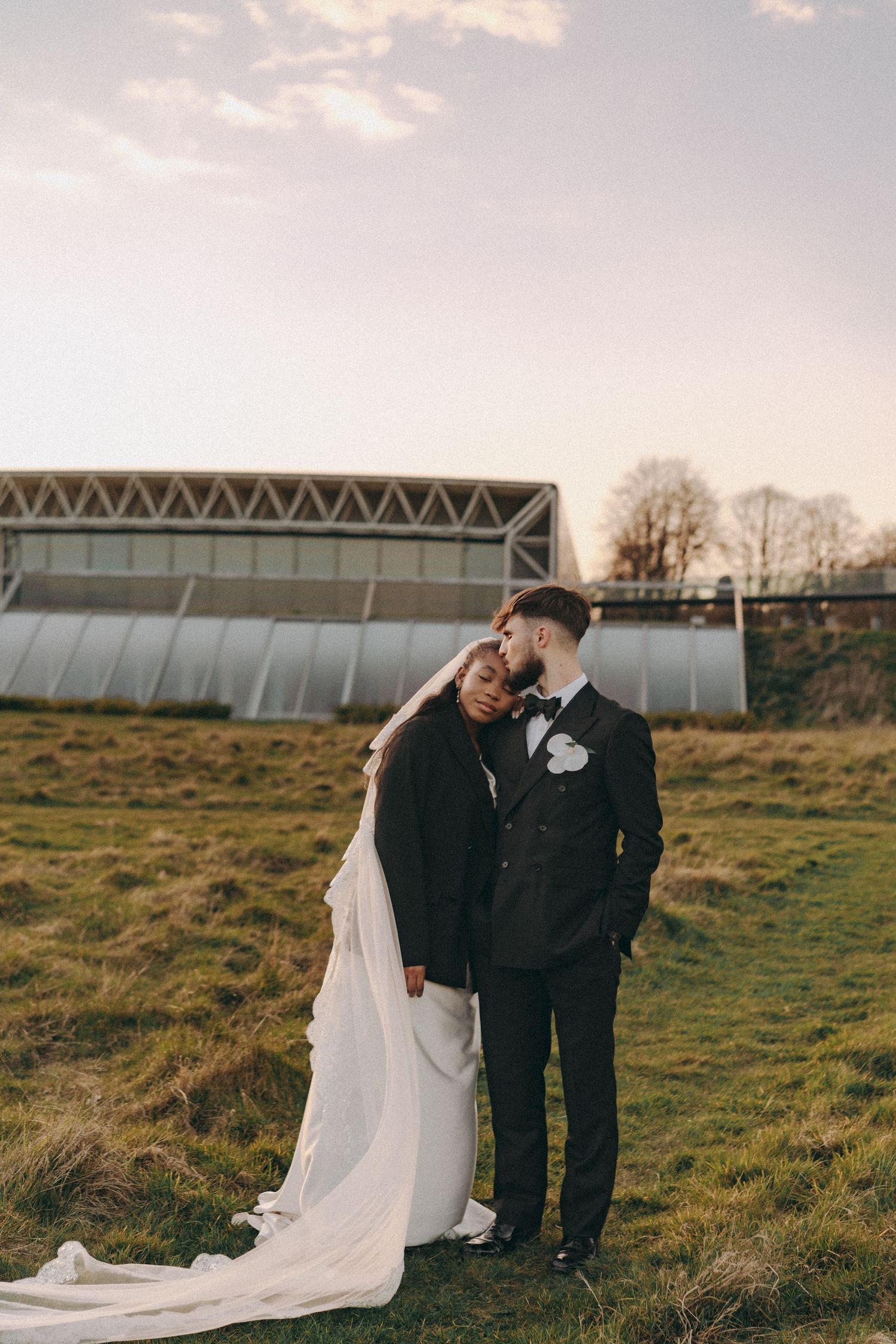 Candid moment between Bride & Groom during sunset hour, bride rests head on groom's shoulder as groom kisses bride's head.