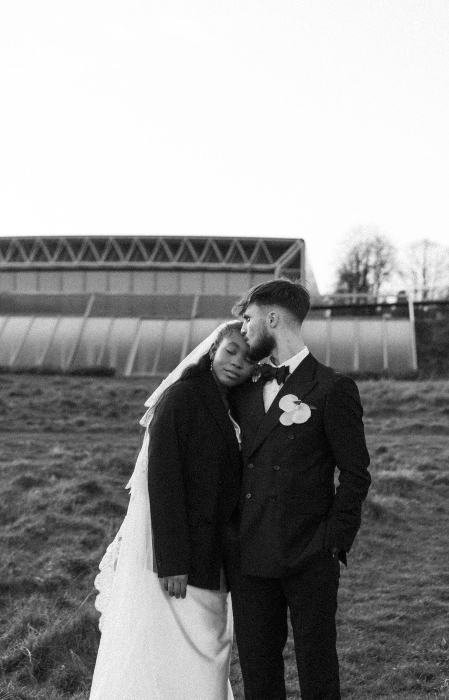 Candid moment between Bride & Groom during sunset hour, bride rests head on groom's shoulder as groom kisses bride's head.