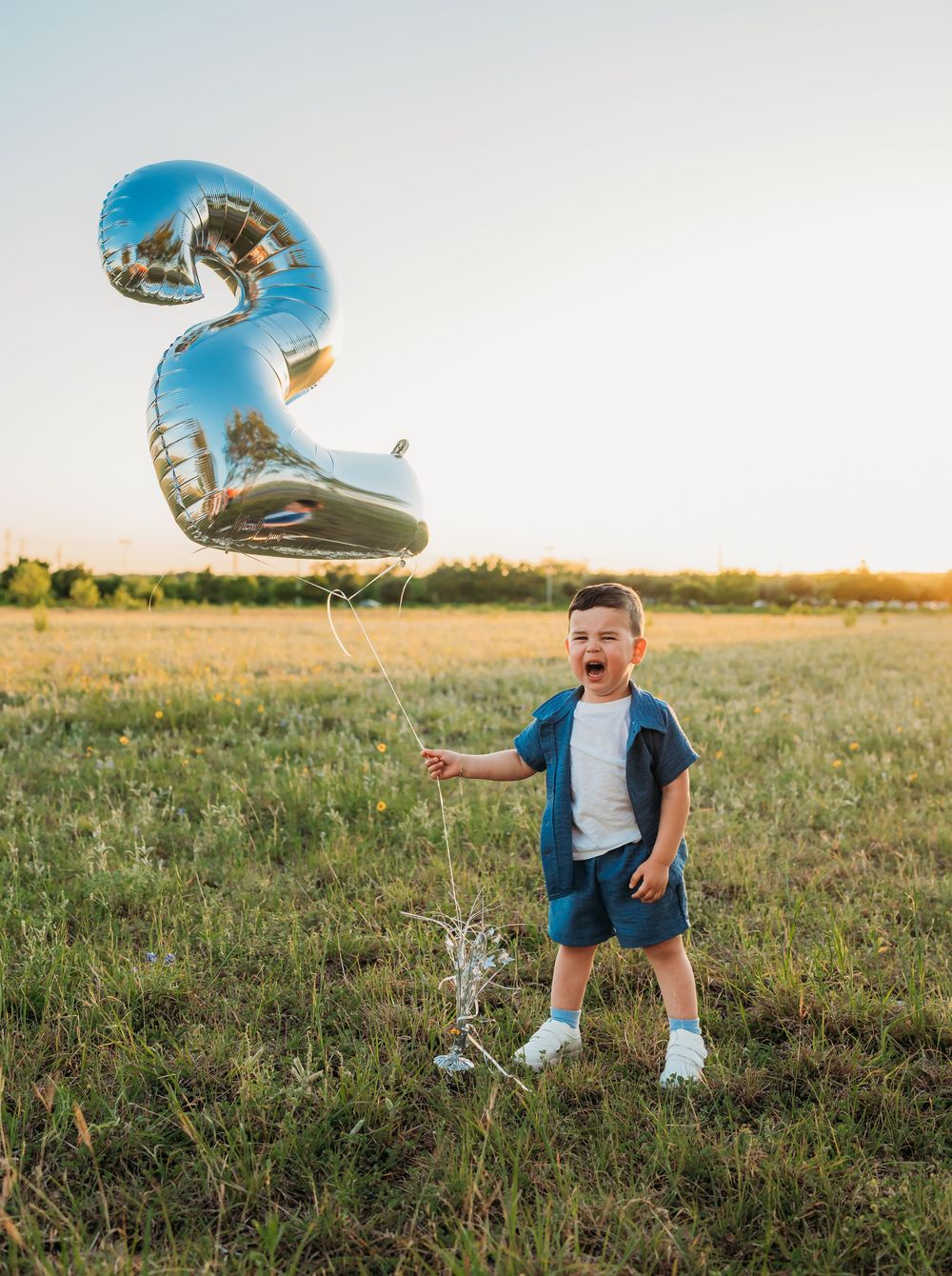 Silver number 2 balloon floating in a grassy field during golden hour sunset.