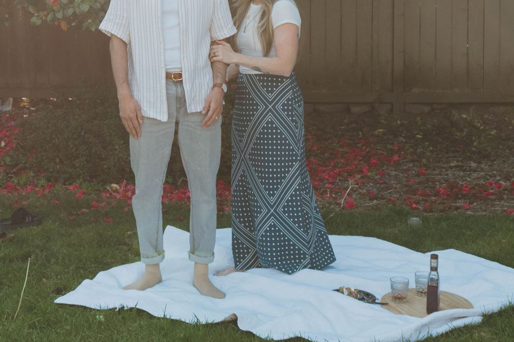 A couple's legs shown standing on a white blanket for a picnic outdoors.