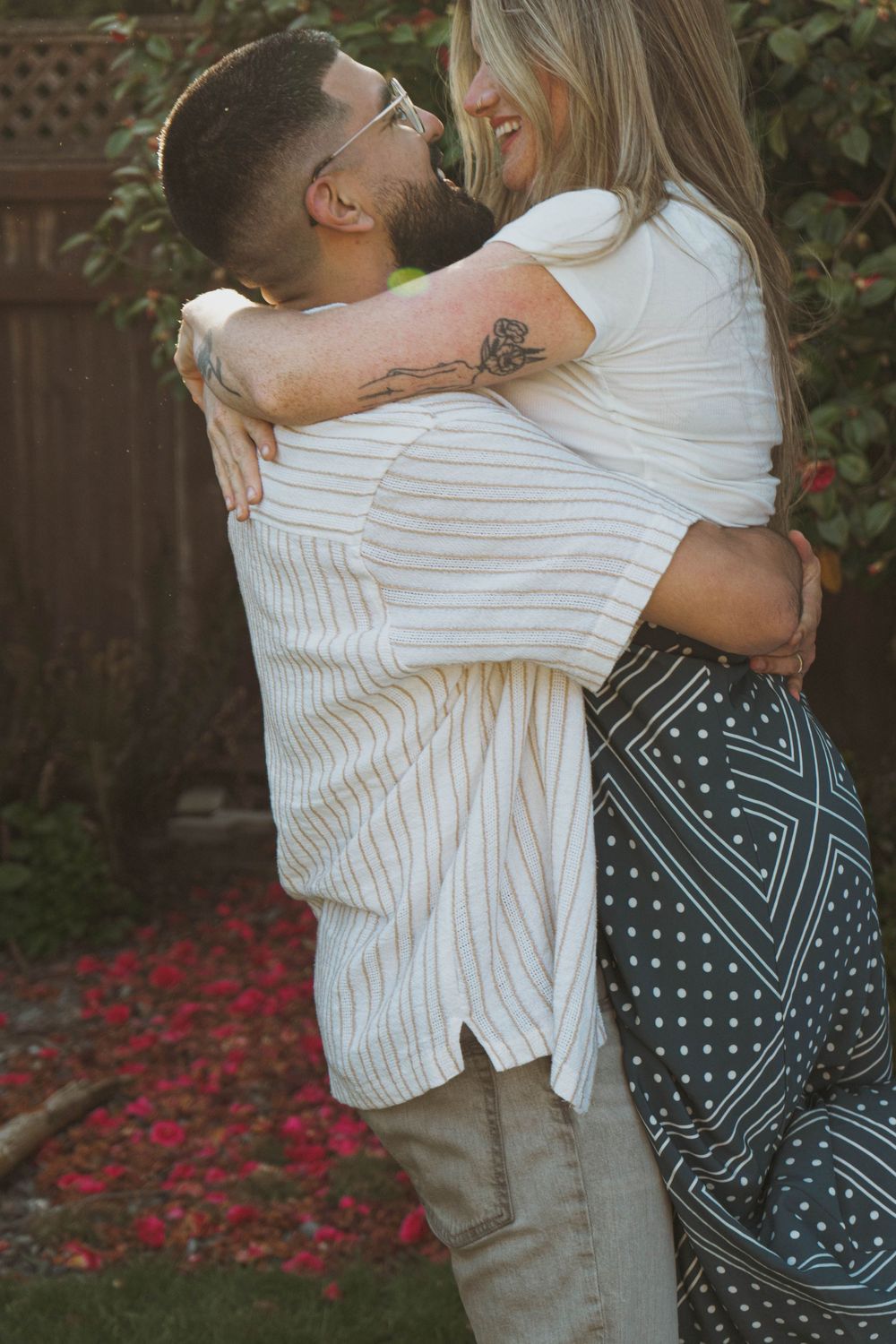A romantic embrace between a couple wearing matching white outfits in a backyard garden setting.