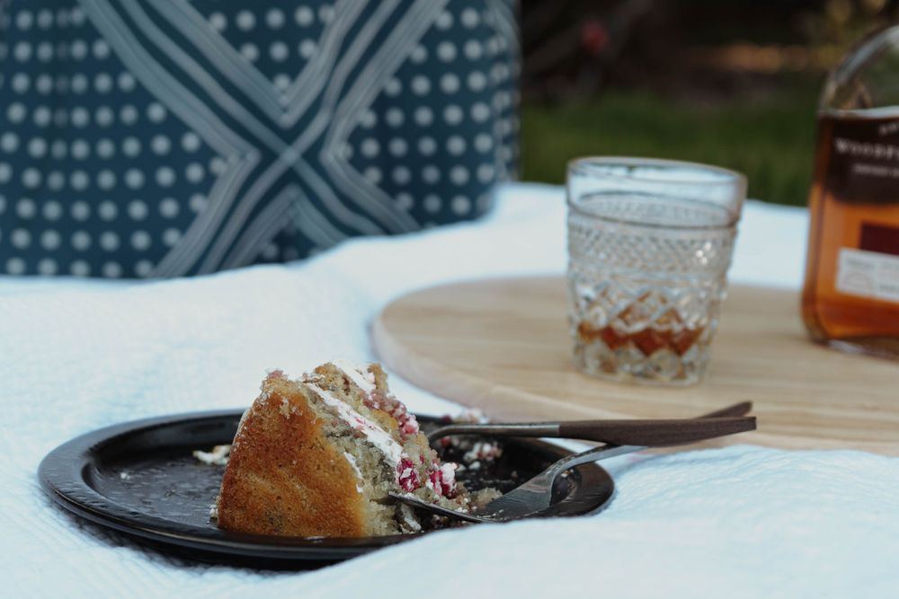A slice of dessert and cocktail glass sit on a table with a patterned cloth.