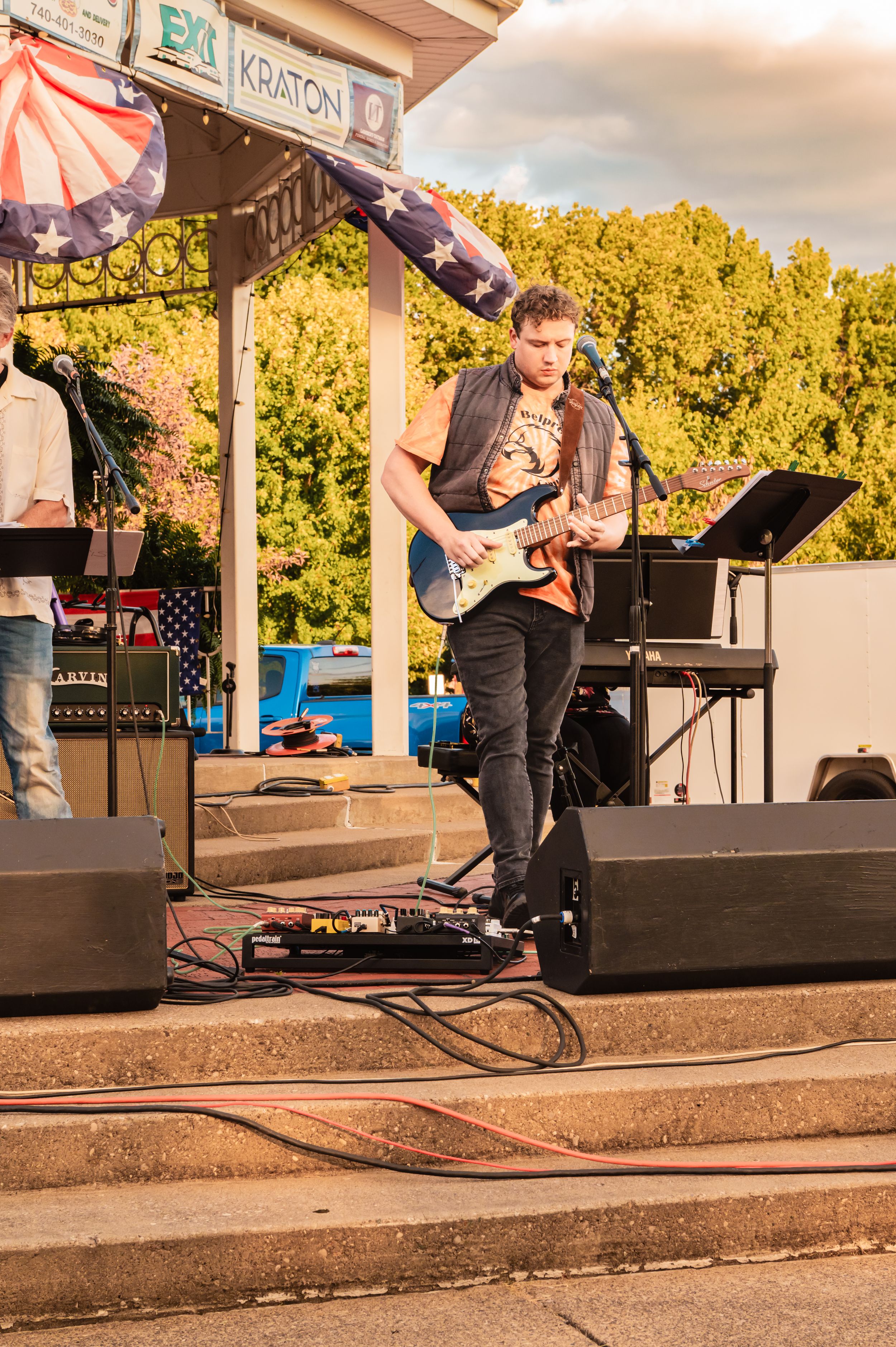 Musicians performing on a covered outdoor stage with string instruments.