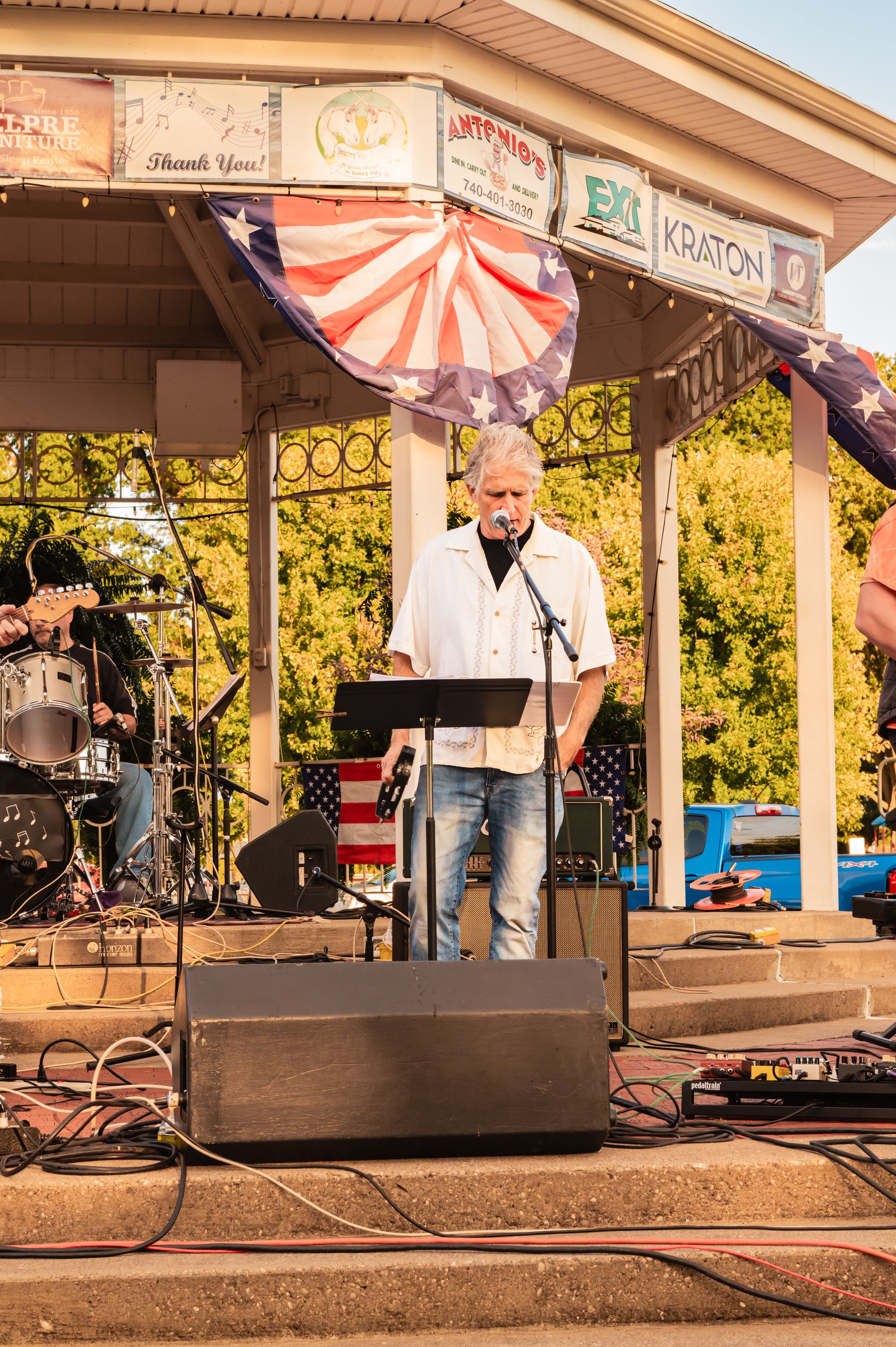Band performing at an outdoor pavilion decorated with American flags.