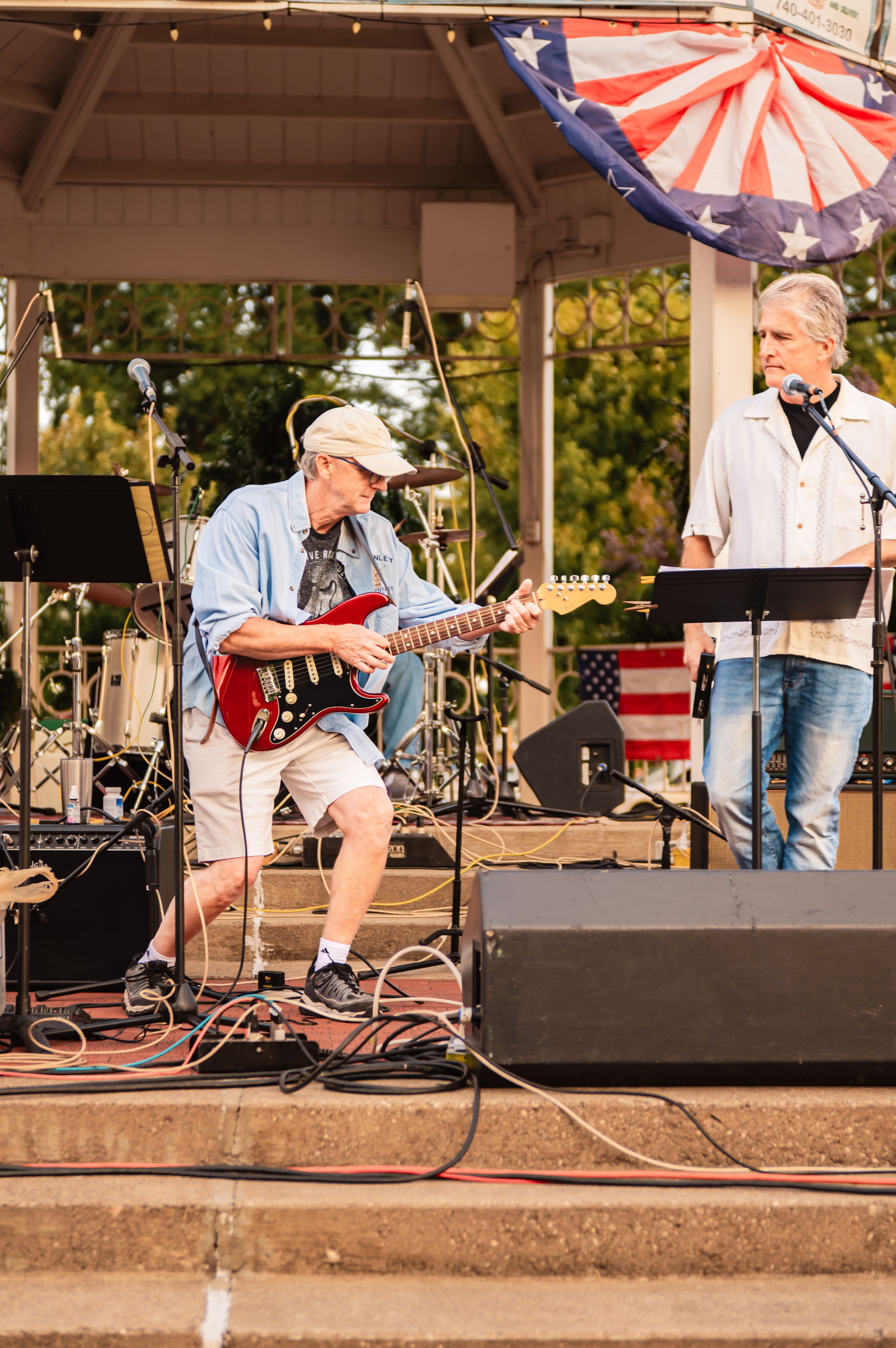 Live band playing instruments on an outdoor stage with American flag decorations.
