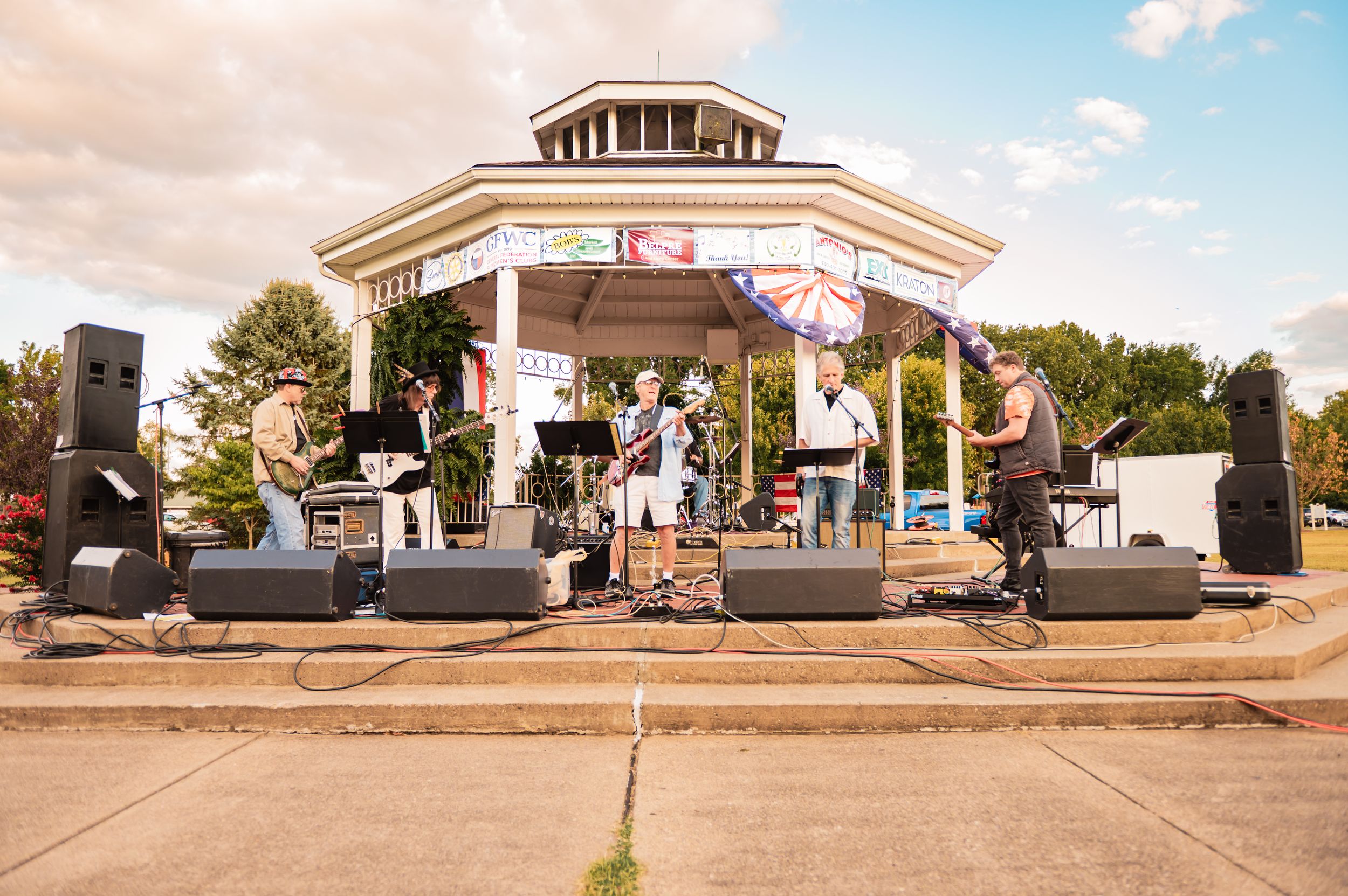 Wide panoramic view of a bandstand concert setup outdoors.