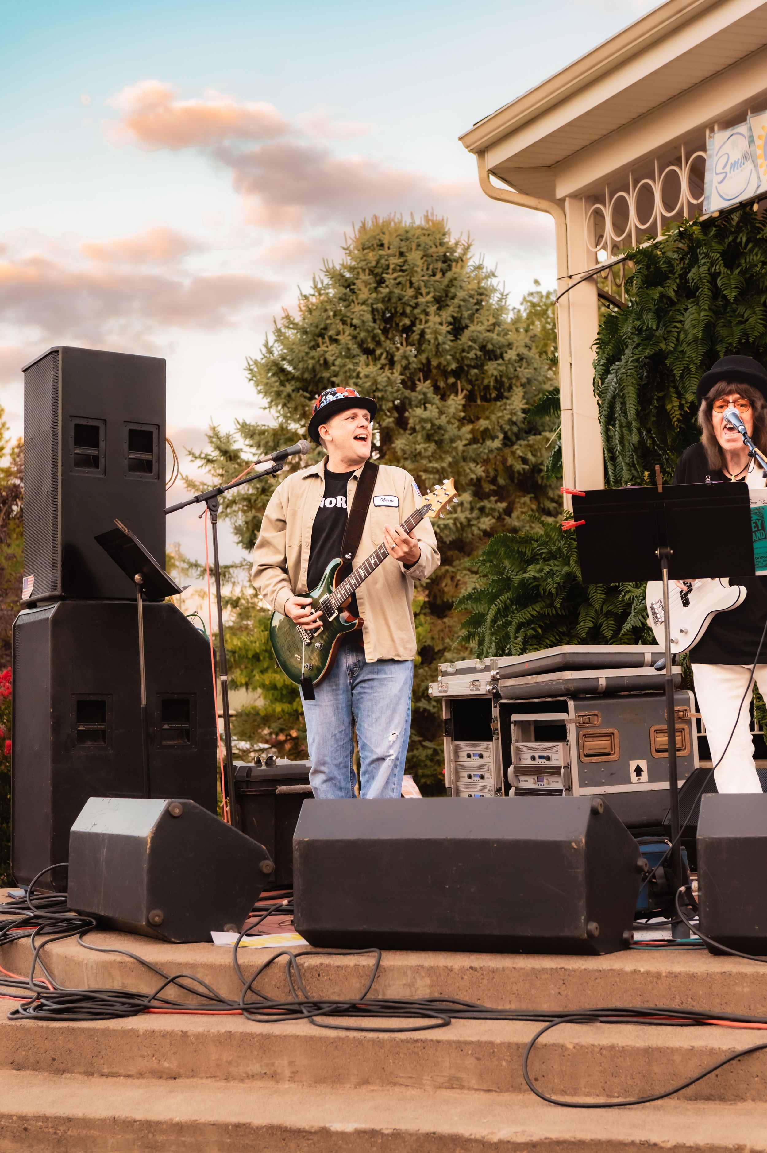 Musicians performing with instruments and sound equipment on outdoor pavilion stage.