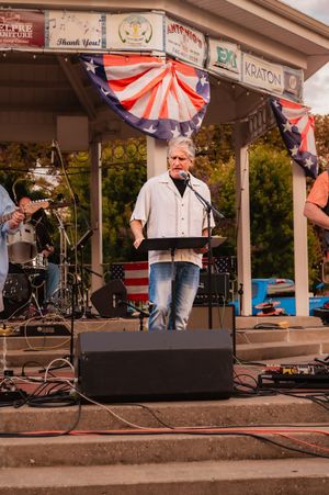 Band performs on gazebo stage with American flag bunting decorations at outdoor event.
