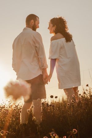 Couple walking hand in hand through a wildflower field at sunset.