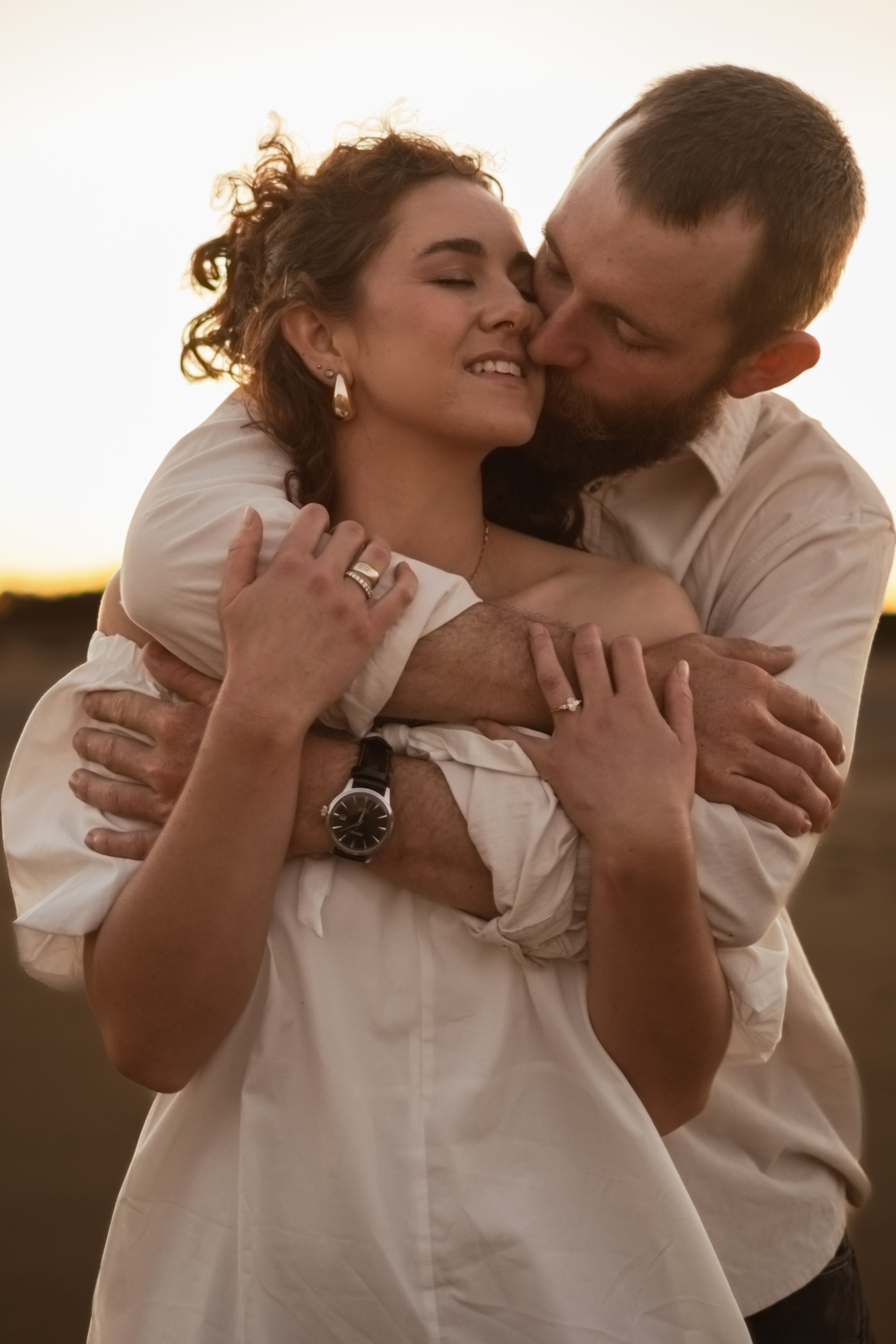 Couple in white clothing share joyful embraces during golden hour.