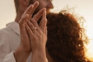 Close-up of hands reaching toward each other during sunset, showing engagement ring.
