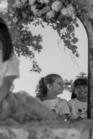 Children share joyful moments under a tree canopy in black and white photography.