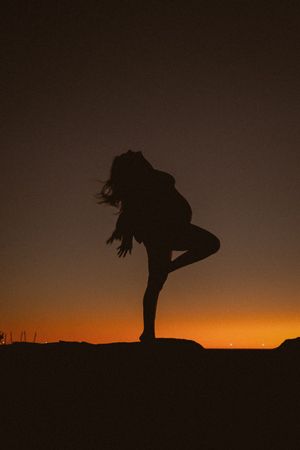 Silhouetted figure performs dynamic movements against a vibrant orange sunset sky.