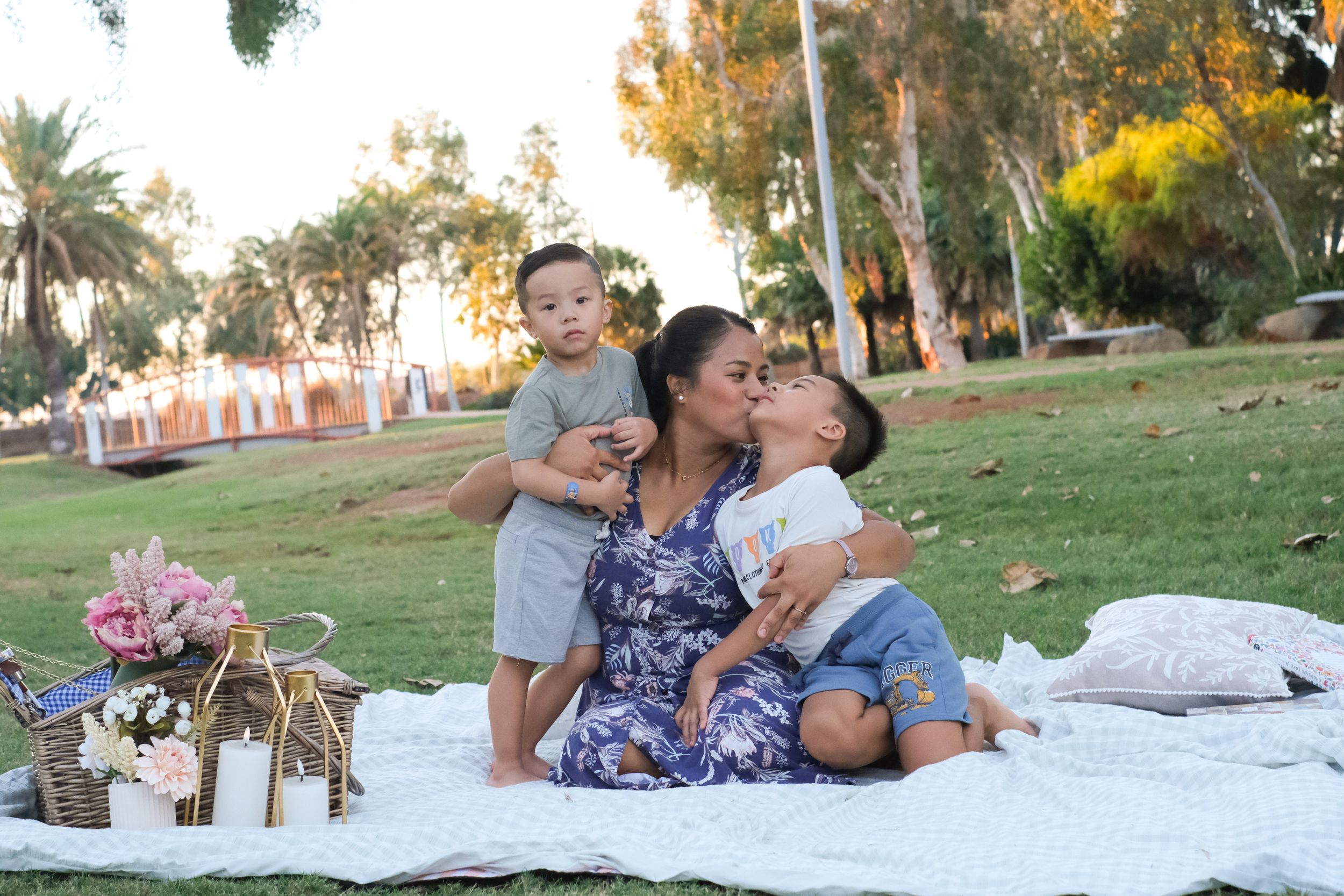Family relaxing together on a picnic blanket in a sunny park setting.