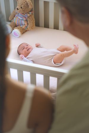 A sleeping baby rests peacefully in a white crib with a teddy bear nearby.
