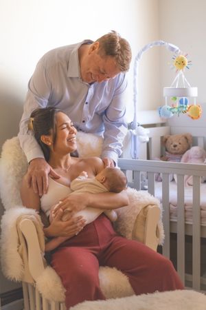 A tender nursery scene shows parents bonding with their newborn baby in a cozy room with a crib.