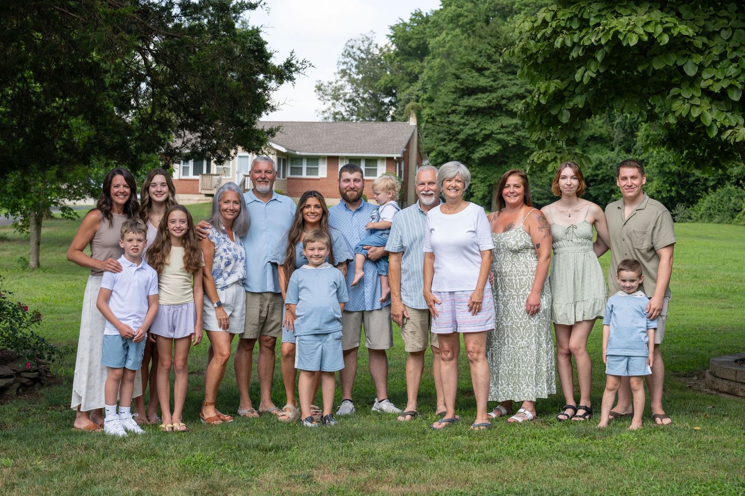 Large family group wearing coordinated light blue and white outfits poses together on a grassy lawn.