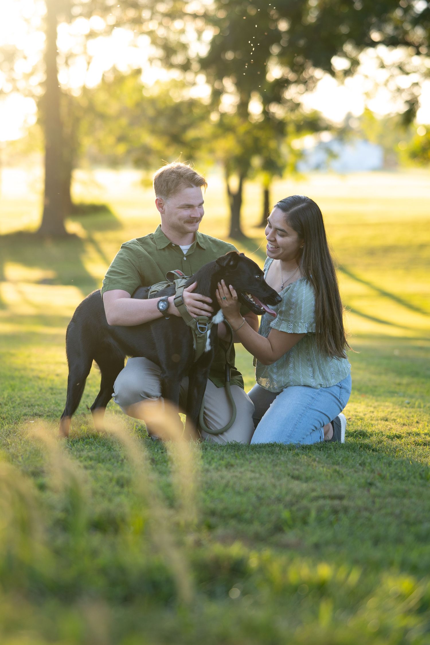 Couple playing with their black dog in a sunny park during golden hour.