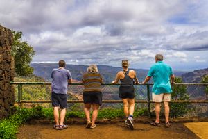 Tourists enjoy scenic mountain views while standing at a lookout railing on a cloudy day.