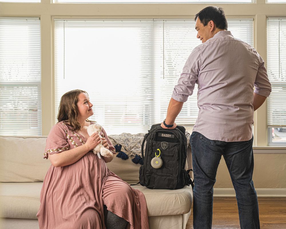 Two people interact with a pet carrier in a bright living room with window blinds.