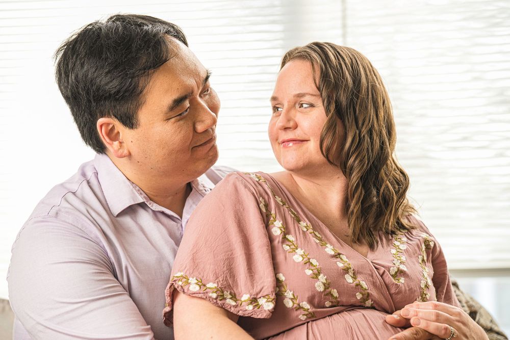 Two people share an intimate moment as they sit close together, with one wearing a pink floral dress.