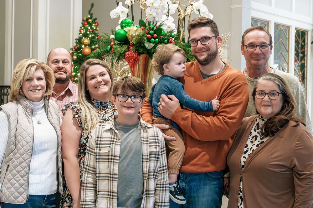 A group poses together in front of holiday decorations with a Christmas tree and floral arrangements visible in background.