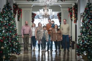 A festive holiday scene with beautifully decorated Christmas trees and a crystal chandelier in an elegant hallway.