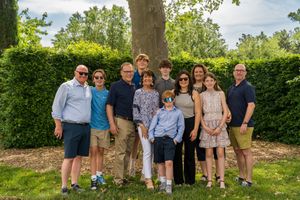 A group stands together outdoors posing for a portrait in a backyard garden with green hedges in the background.