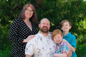 Happy family of four poses together outdoors against lush green foliage background.