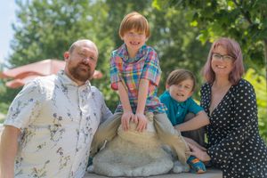 A family poses together outdoors near a stone pillar on a sunny summer day.