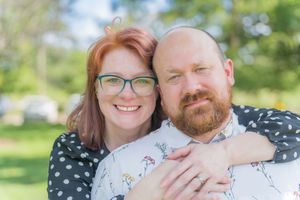 Close-up portrait of two people embracing outdoors on a sunny day with green background.