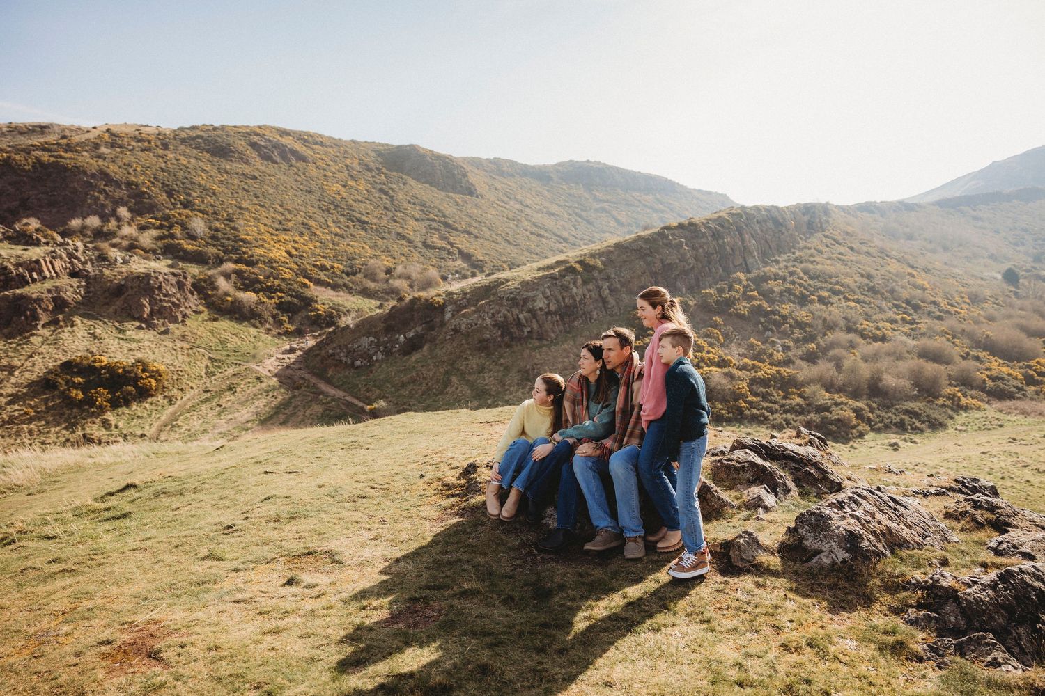 A group sits together on rocks enjoying scenic mountain views on a sunny hillside in nature.