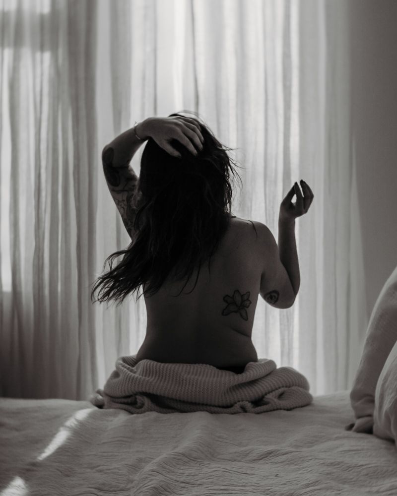 Artistic black and white photo of a person sitting on bed with flowing hair movement.