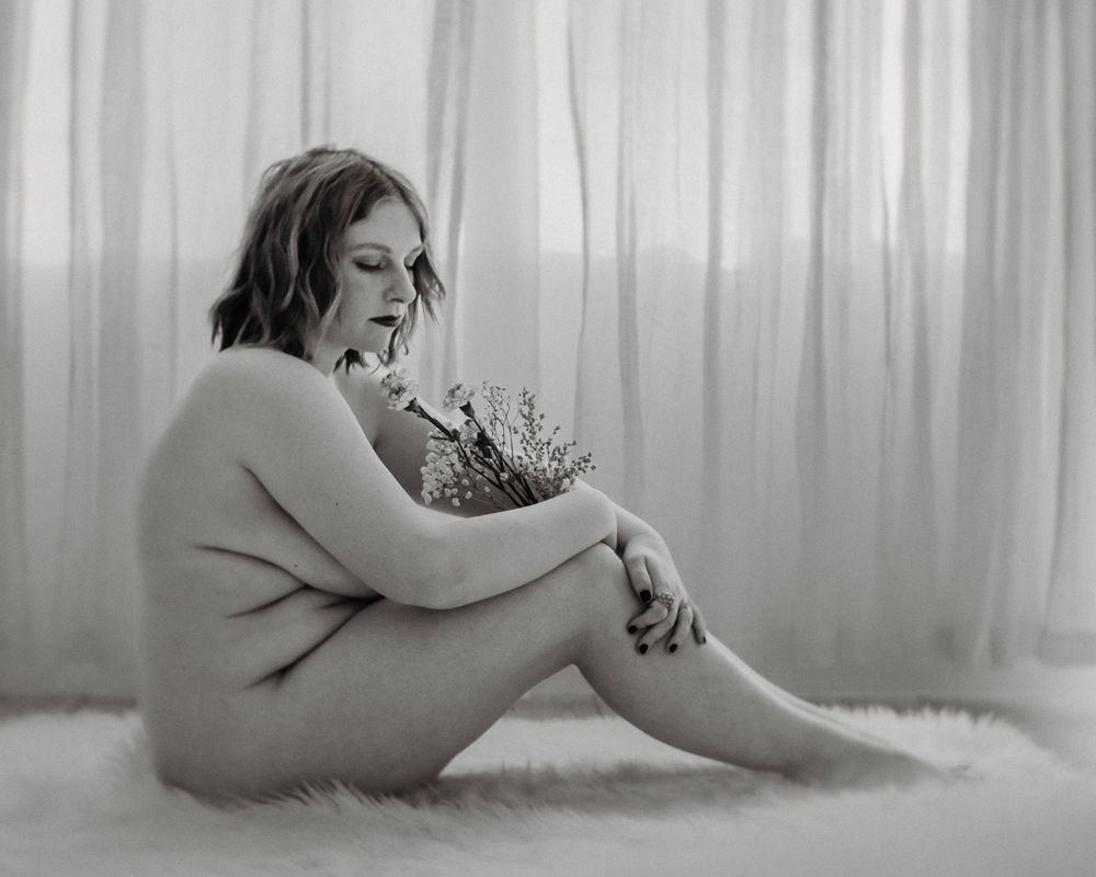 Intimate black and white portrait with flowers in soft window light.