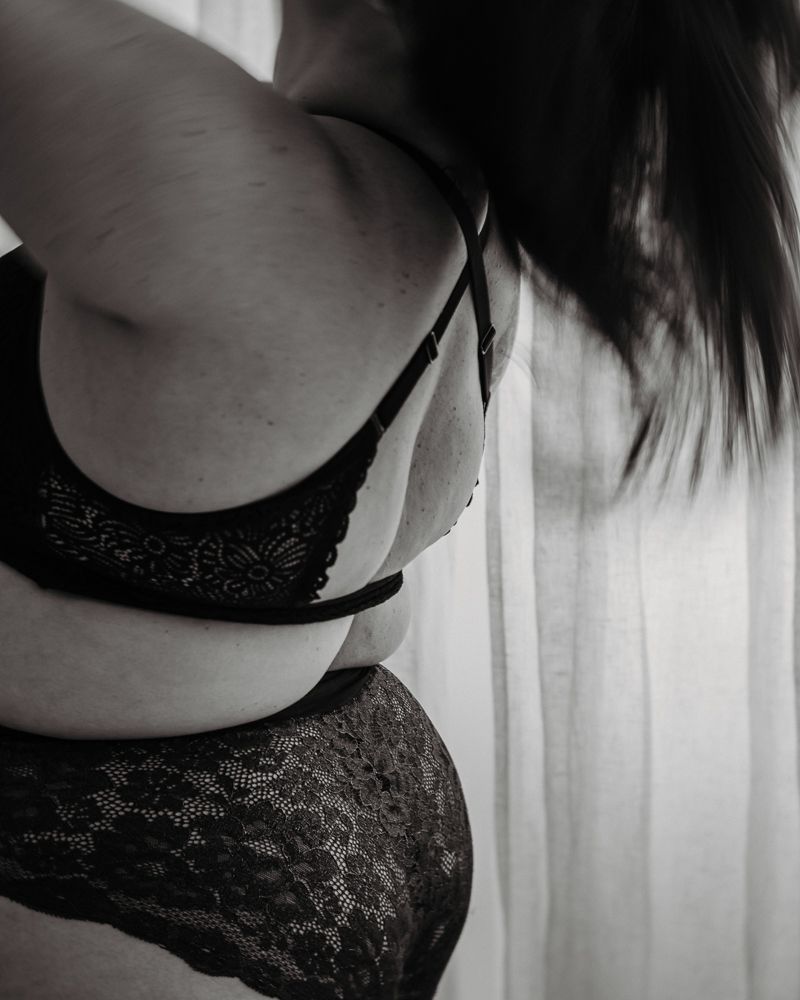 Close-up black and white photo of black lace lingerie against sheer curtain background.