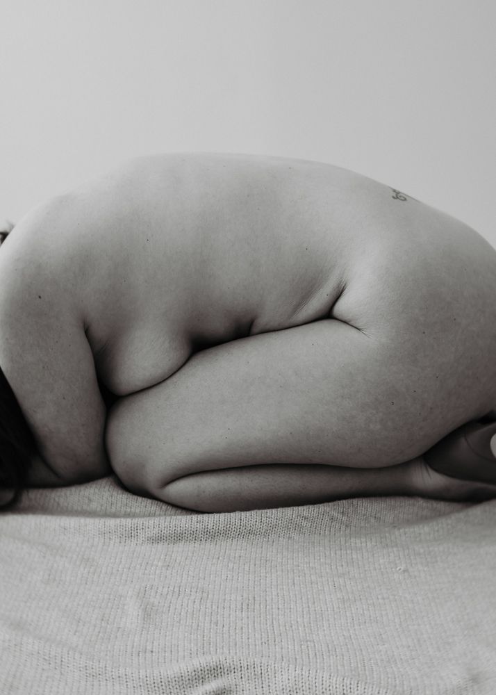 Abstract nude form curled on textured surface in monochrome.