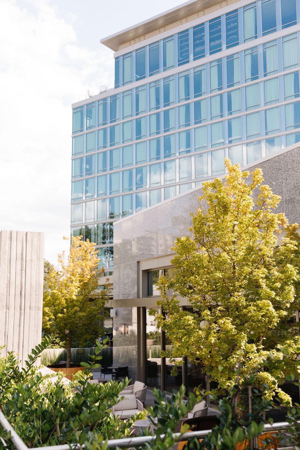 Modern glass office building exterior with yellow autumn trees and landscaped garden area in foreground.