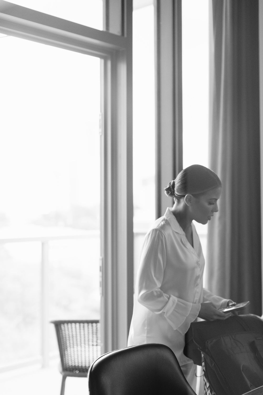 A stylish black and white portrait of a person in a white button-down shirt standing by a bright window.
