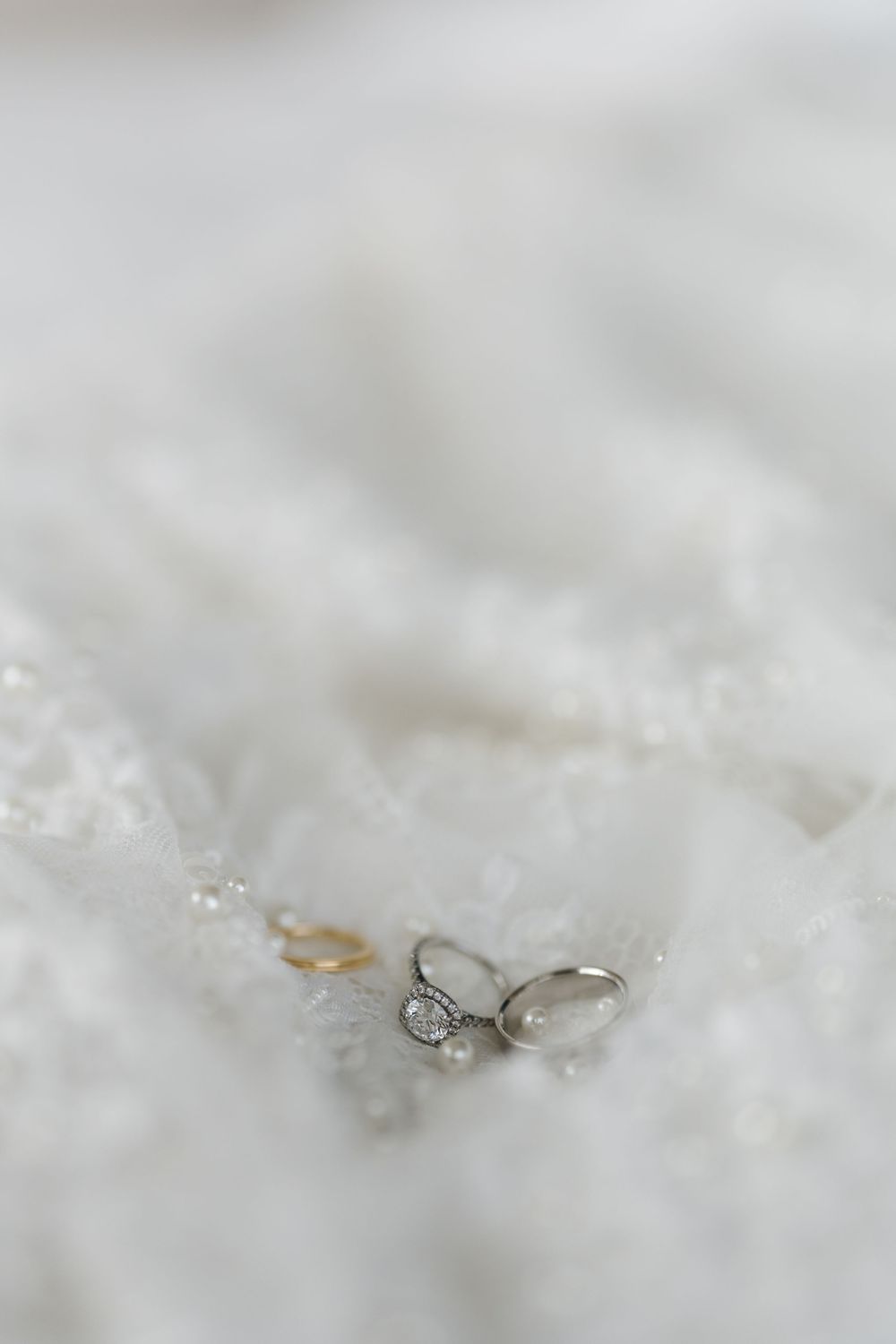 Wedding rings placed on delicate white lace fabric with shallow depth of field highlighting the diamond details.