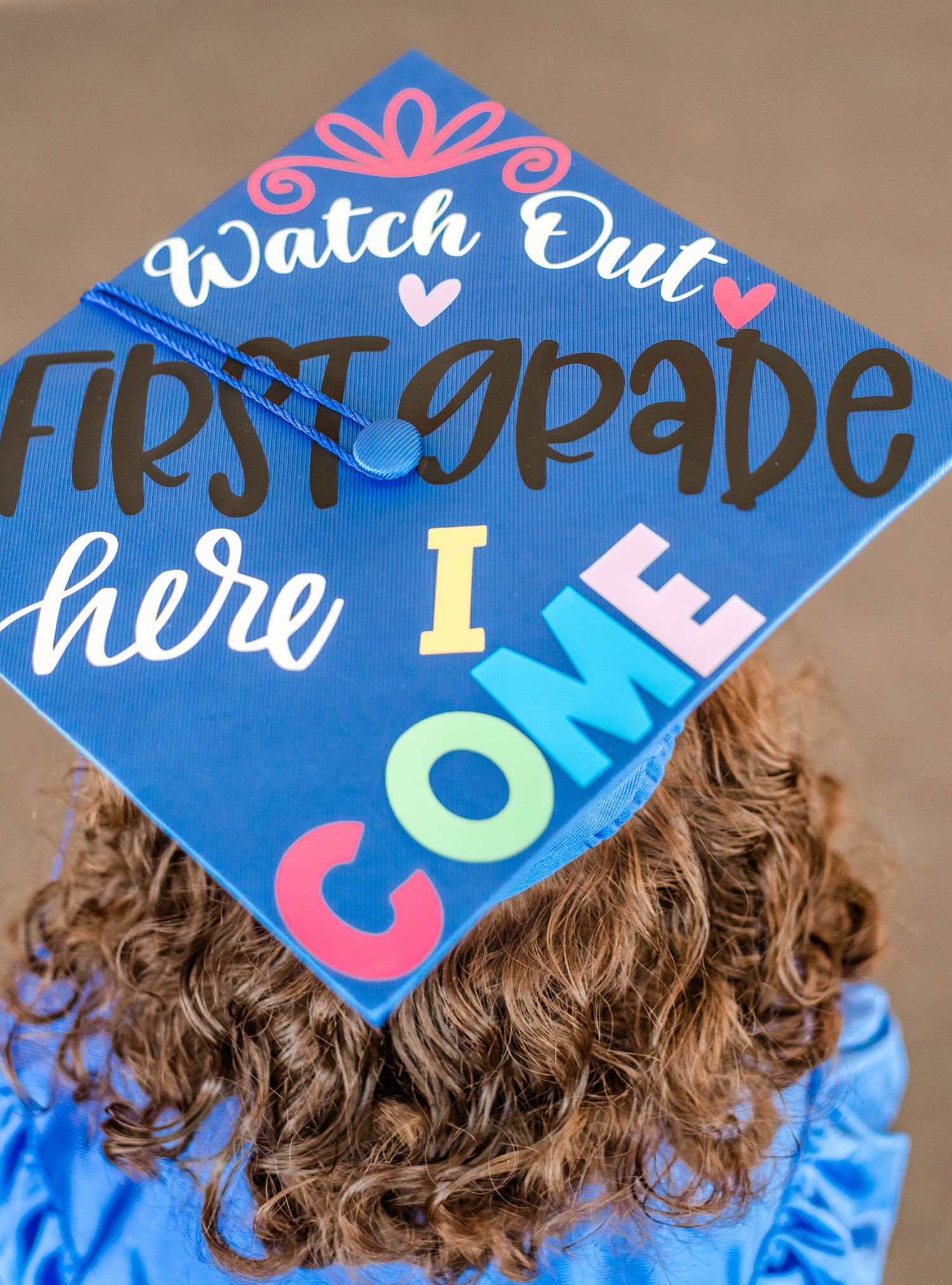 A decorated graduation cap in bright blue features colorful text and decorative elements.
