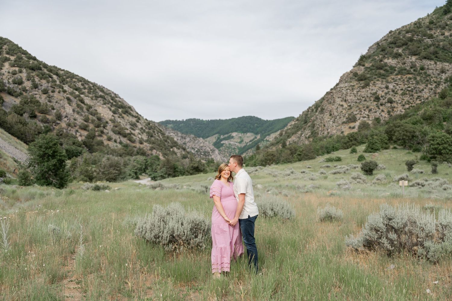 A couple stands together in a scenic mountain valley with sagebrush and rolling hills in Logan, Utah.