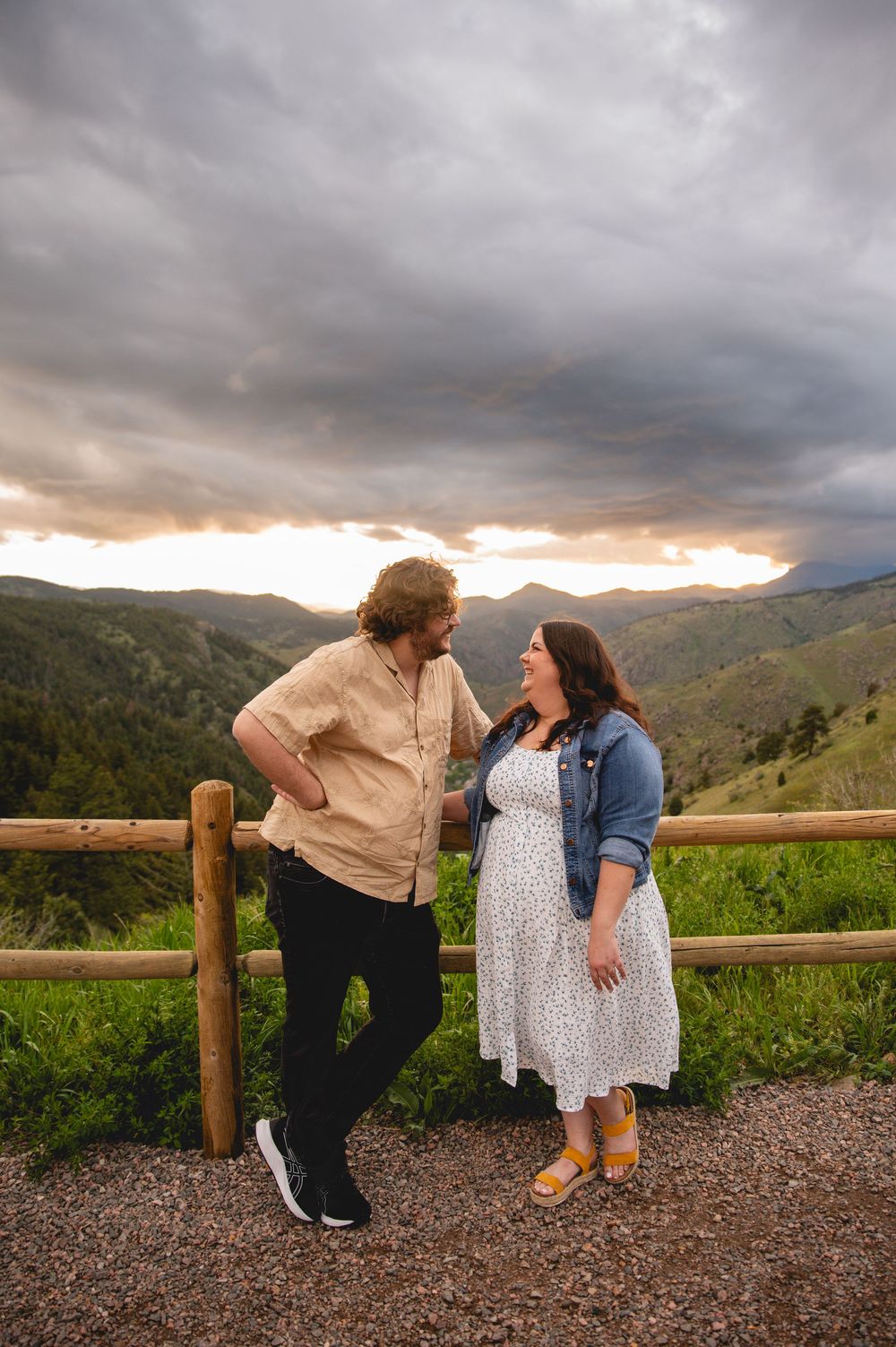 A couple shares a tender moment at sunset against a mountain backdrop with dramatic storm clouds overhead.
