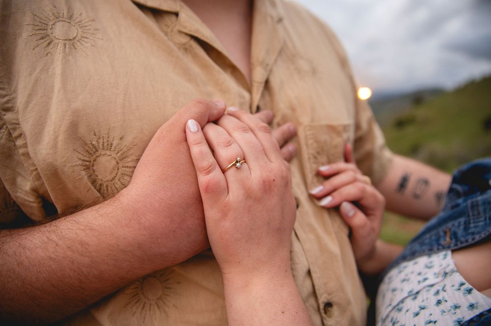 Close-up of hands resting against a tan button-up shirt with embroidered sun patterns outdoors.